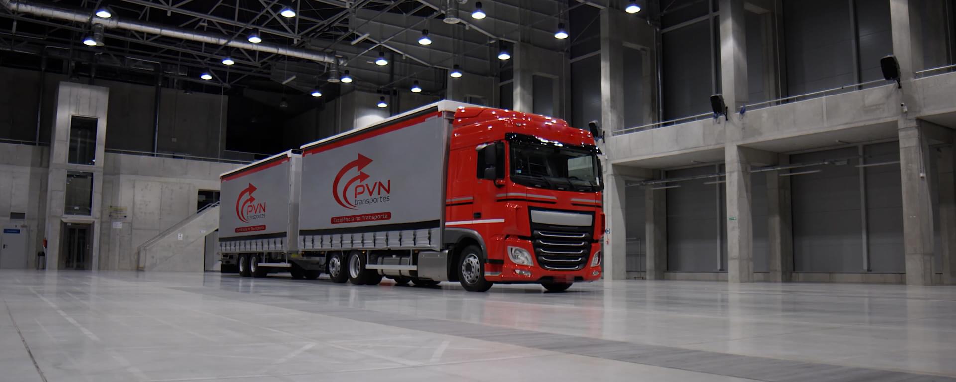 Caminhão Vermelho em um galpão, com duas cargas customizadas com a logo da PVN Transportes